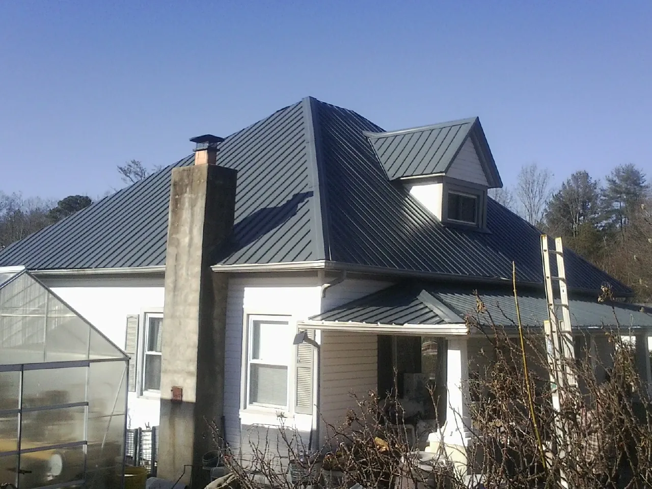 Dark blue standing seam metal roof on a white farmhouse with dormer — Slate & Tile Roof Repair by Roofing Brothers in Hansen
