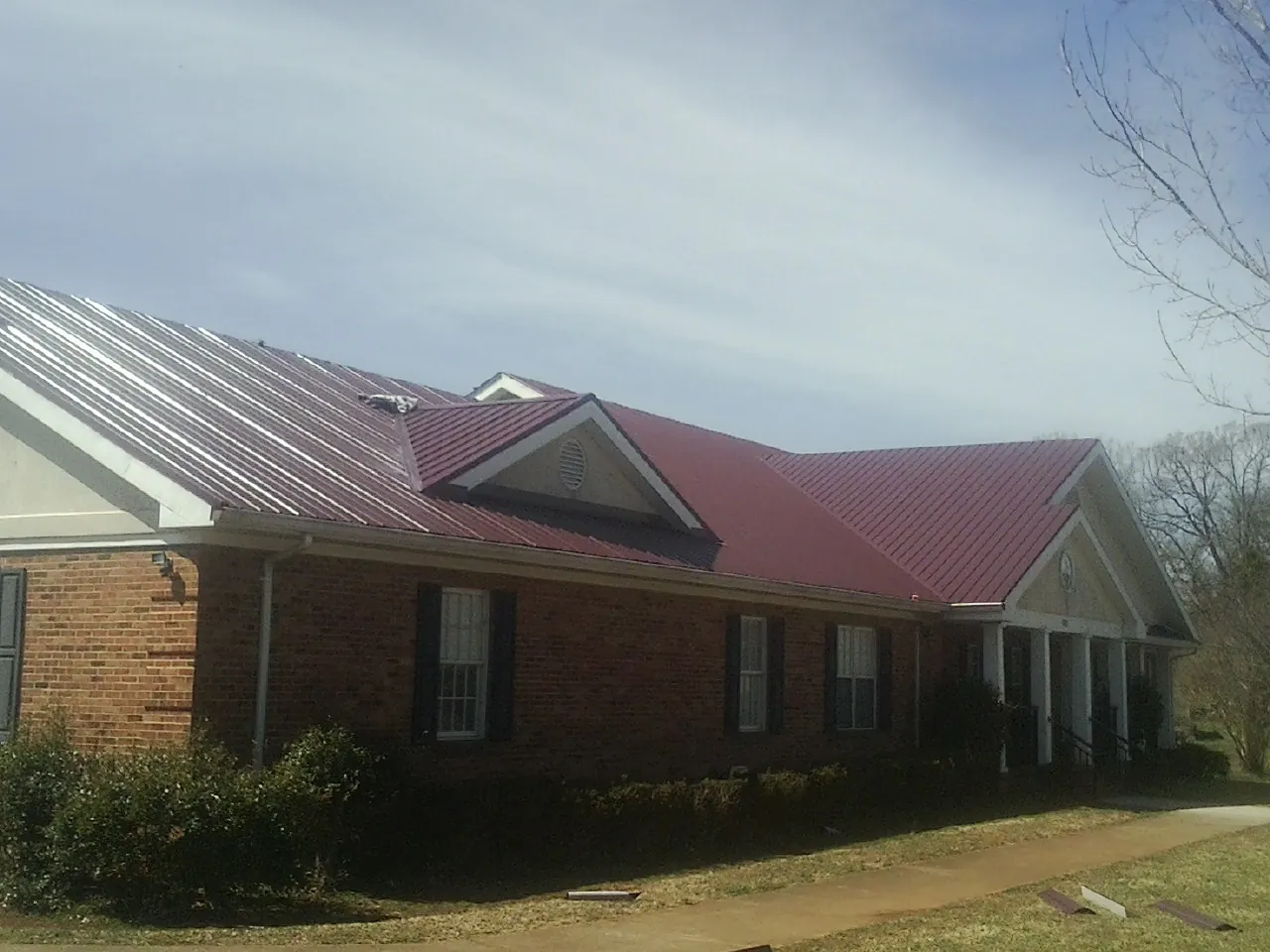 Red metal roof with gabled entries on a long brick building, from a Hail Damage Roof Repair job in Hansen