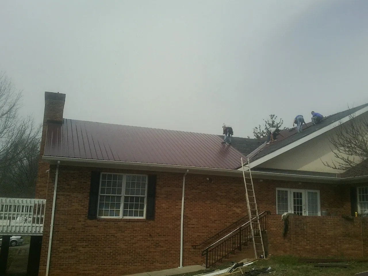 Crew setting red metal roofing panels on a brick home in Hansen