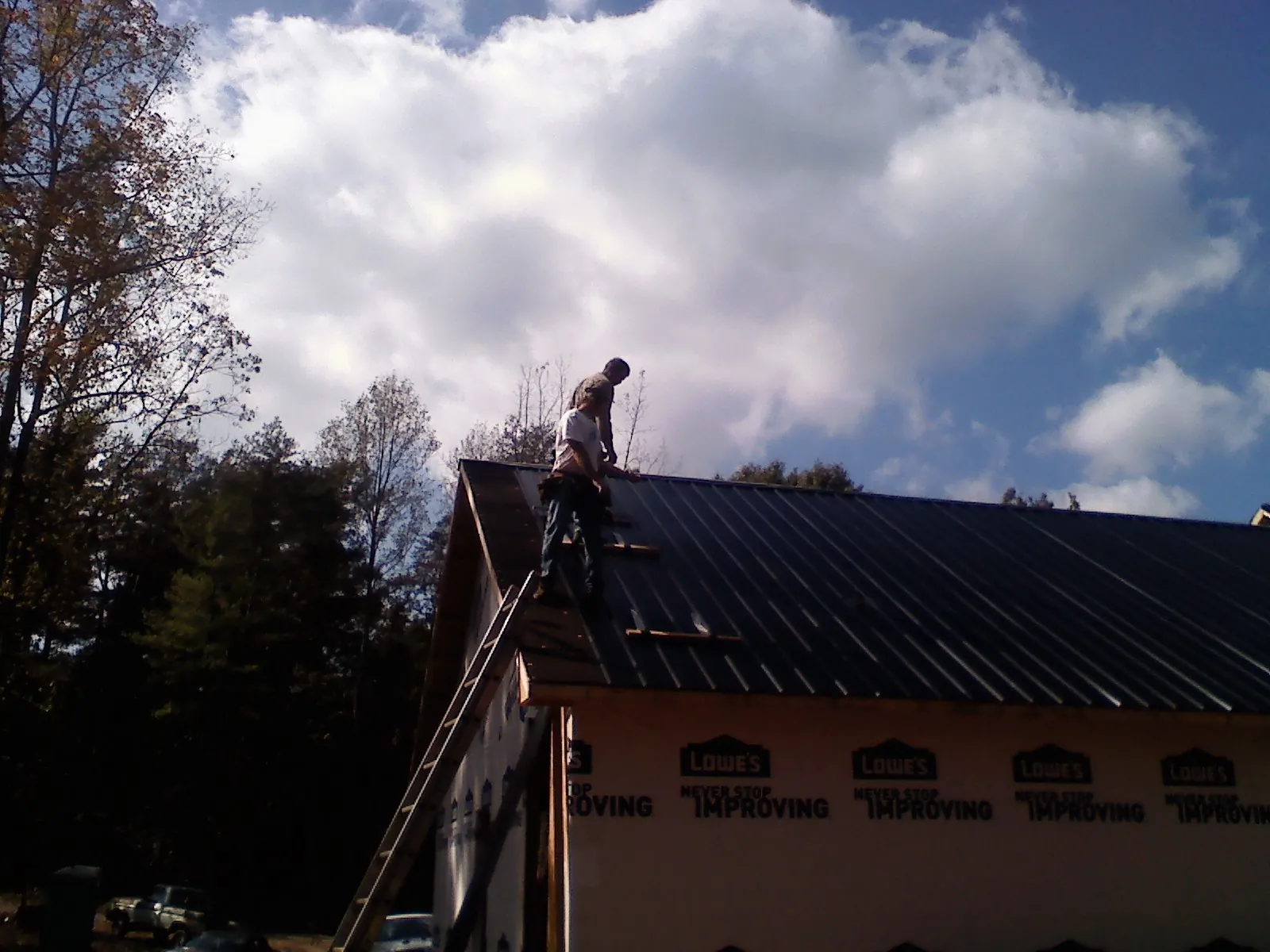 Roofer fastening dark metal panels high against a cloudy sky, from a Roof Inspection job in Hansen